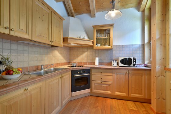 Küche im Appartement Wilder Kaiser Rustikale Holzküche mit Einbaugeräten, gefliester Arbeitsplatte und Holzboden unter einer Dachschräge.