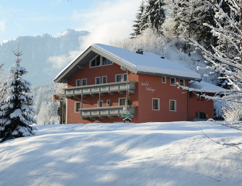 Gasthof Möllinger im Winter Ein rotes, schneebedecktes Gasthaus mit Holzbalkonen in einer winterlichen Berglandschaft.