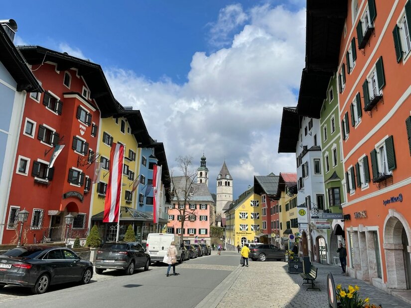 Blick durch eine Straße mit bunten Häuserfassaden auf einen Kirchturm in Kitzbühel.