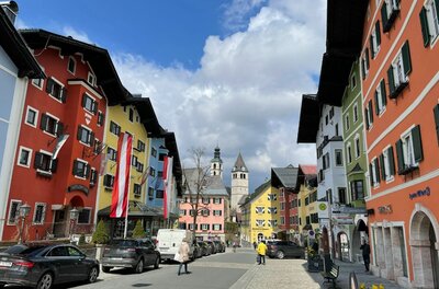 Blick durch eine Straße mit bunten Häuserfassaden auf einen Kirchturm in Kitzbühel.