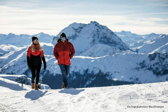 Winterwandern in den Kitzbüheler Alpen Zwei Personen in Winterkleidung wandern auf einem verschneiten Bergpfad vor einem alpinen Panorama.