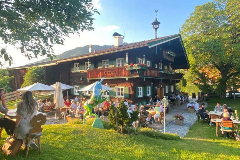 Wirtshaus zum Rehkitz Traditionelles Holzhaus mit Außengastronomie auf einer grünen Wiese unter blauem Himmel.