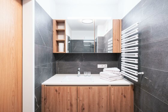 Ein modernes Badezimmer mit Holz- und Steinakzenten. Es enthält ein Waschbecken, Handtücher und einen Spiegel.
