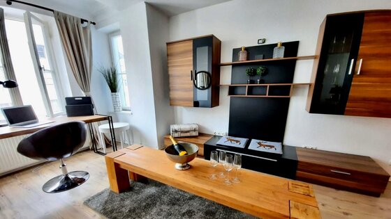 Modernes Wohnzimmer mit Holzmöbeln, Schreibtisch am Fenster und Sektkühler auf dem Couchtisch.