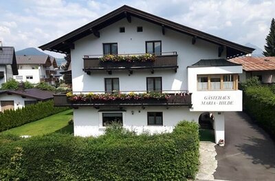 Vorderansicht eines weißen Gästehauses mit dunklen Holzbalkonen und Blumenschmuck.