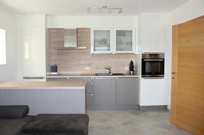 Moderne Einbauküche mit grauen Fronten, Holzrückwand, Backofen und Kochinsel.
