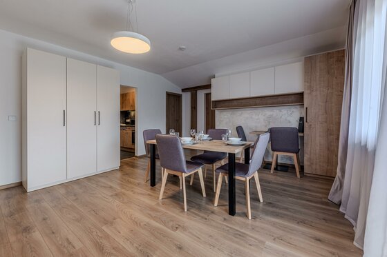 Moderner Essbereich mit Holztisch, grauen Polsterstühlen und weißen Einbauschränken in einem Apartment.
