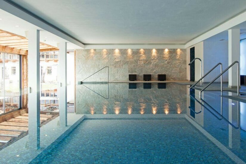 Modernes Hallenbad mit Natursteinwand, Metallgeländern und blauem Mosaikbecken.