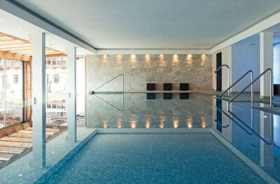 Hallenbad im Kitzhof Resort Modernes Hallenbad mit Natursteinwand, Metallgeländern und blauem Mosaikbecken.