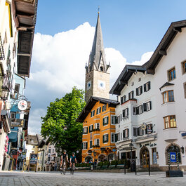 Eine malerische Straße in Kitzbühel mit bunten Gebäuden und einer markanten Kirchturmspitze im Hintergrund.