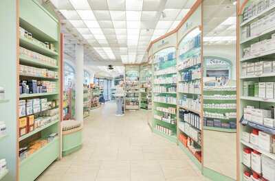 Innenansicht einer hellen Apotheke mit grünen Regalen und zahlreichen Pflegeprodukten.