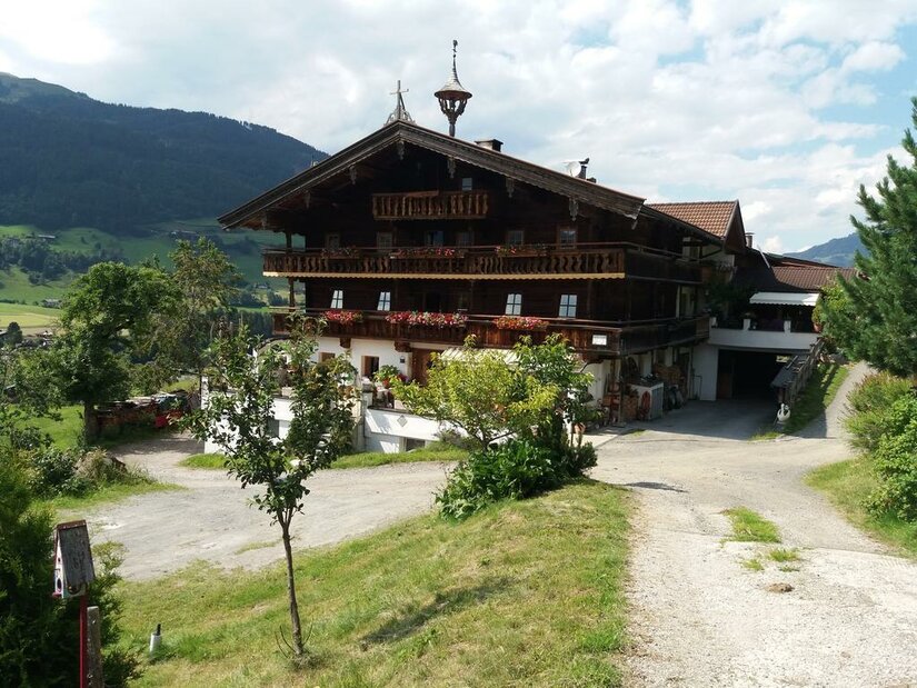 Talhof im Sommer Großes, mehrstöckiges Holzhaus im alpinen Stil mit Blumenbalkonen vor bewaldeten Bergen.