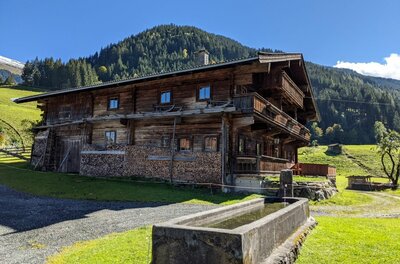 Ein traditionelles Holzhaus in den Alpen mit einem steinernen Brunnen im Vordergrund.