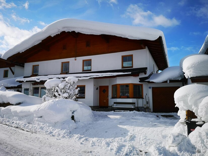 Winteransicht Haus Aschenwald Zweistöckiges Wohnhaus mit holzverkleidetem Giebel und einer dicken Schneeschicht auf dem Dach.