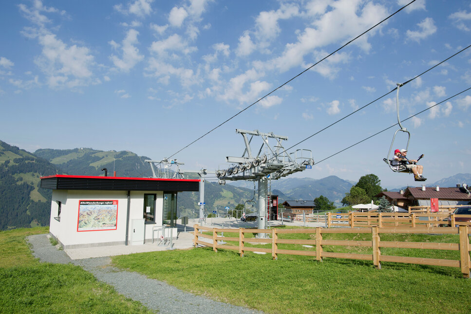 Eine Seilbahnstation mit einem modernen Gebäude und einem Fahrstuhl, der über grüne Wiesen in die Berge führt.