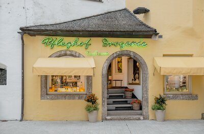 Fassade der Pfleghof Drogerie mit gelber Wand, grüner Leuchtschrift und Rundbogen-Eingang.