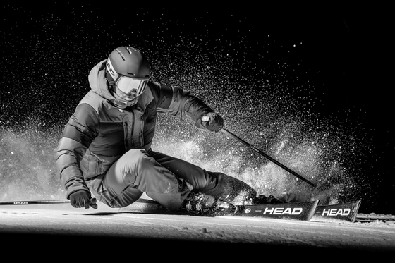 Ein Skifahrer fährt in der Nacht auf einer schneebedeckten Piste. Der Schnee spritzt um ihn herum und es herrscht eine dynamische Atmosphäre.