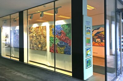 Galerie Kitz Art Eine Kunstgalerie mit großen, farbenfrohen Gemälden an der Wand. Die Fenster sind klar, und es gibt zusätzliche Kunstwerke in Rahmungen auf der rechten Seite.