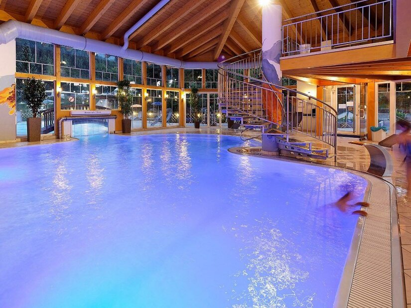 Wellness-Center "Energiebrunnen" Ein modernes Hallenbad mit leuchtend blauem Wasser und einer Rutsche. Große Fenster sorgen für viel Tageslicht und eine entspannende Atmosphäre.