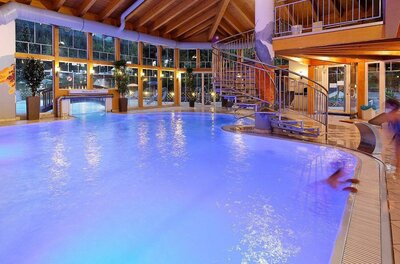 Wellness-Center "Energiebrunnen" Ein modernes Hallenbad mit leuchtend blauem Wasser und einer Rutsche. Große Fenster sorgen für viel Tageslicht und eine entspannende Atmosphäre.
