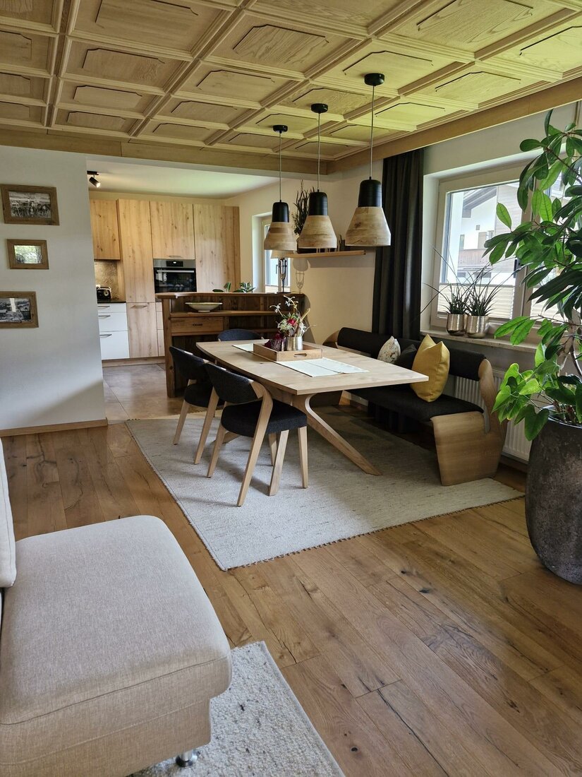 Moderner Essbereich mit Holztisch, Sitzbank und Stühlen unter einer Kassettendecke aus Holz.