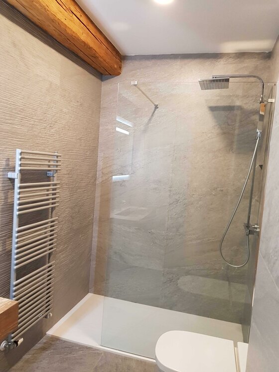 Modernes Badezimmer mit begehbarer Glasdusche, Handtuchheizkörper und Holzbalken an der Decke.