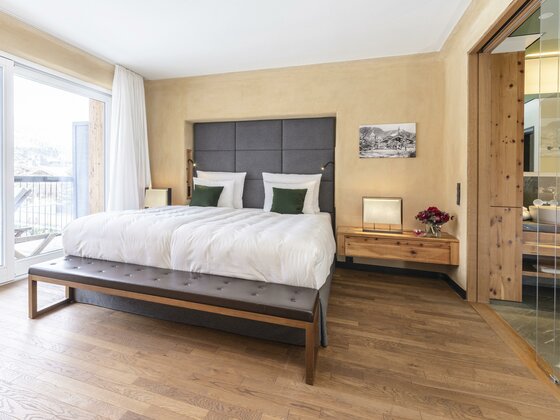 Doppelzimmer Kitzbühel Residences Modernes Hotelzimmer mit Doppelbett, gepolstertem Kopfteil, Parkettboden und Blick ins angrenzende Badezimmer.