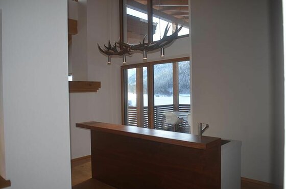Moderner Tresen aus dunklem Holz mit einer Geweih-Leuchte vor einem Fenster mit Bergblick.