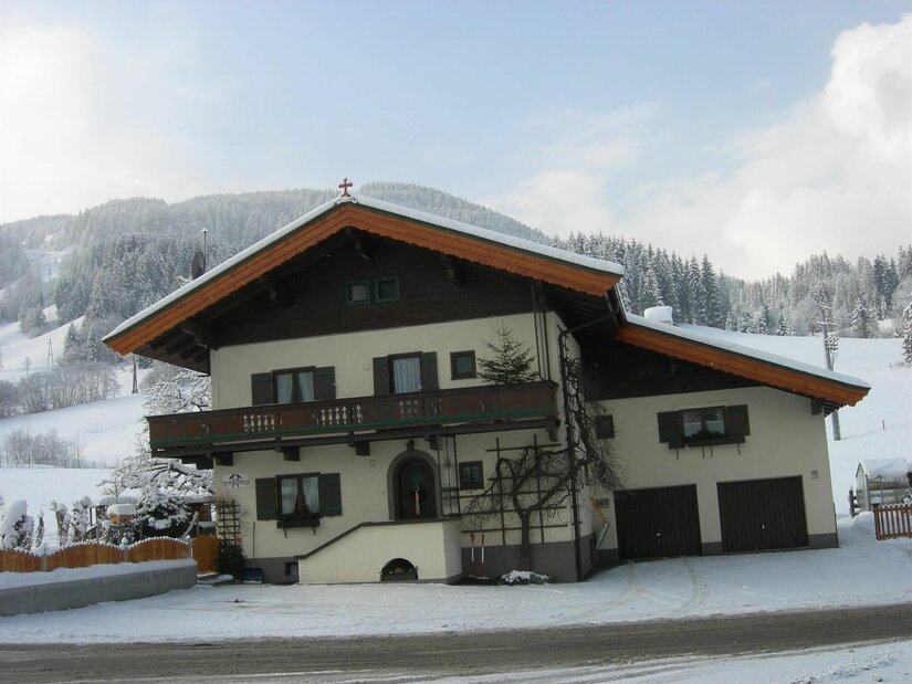 Zweistöckiges Alpenhaus mit Holzbalkon und Satteldach in einer verschneiten Berglandschaft.