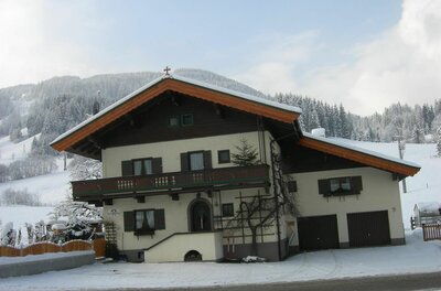 Zweistöckiges Alpenhaus mit Holzbalkon und Satteldach in einer verschneiten Berglandschaft.