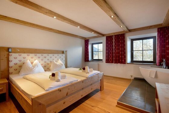 Schlafzimmer mit Badewanne Schlafzimmer mit Doppelbett aus Holz, Holzbalkendecke und einer freistehenden Badewanne am Fenster.