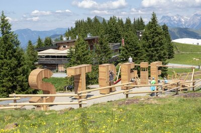 Sommererlebnis Streif Große Holzbuchstaben des Wortes STREIF als Spielstationen auf einer Almwiese vor einer Berghütte.