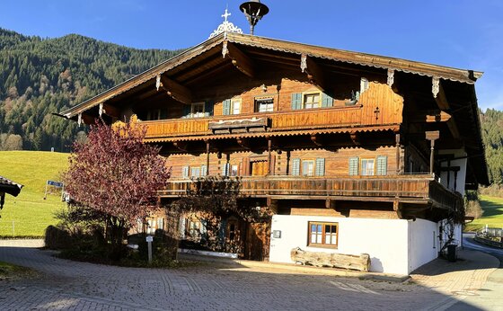 Neuhaus Ein traditionelles Holzhaus in malerischer Umgebung. Im Hintergrund erheben sich grüne Hügel und Bäume.