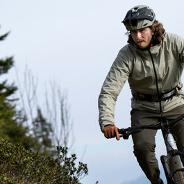 Ein Mountainbiker fährt in Kitzbühel mit konzentriertem Gesichtsausdruck durch eine bewaldete Landschaft, umgeben von grünen Sträuchern.