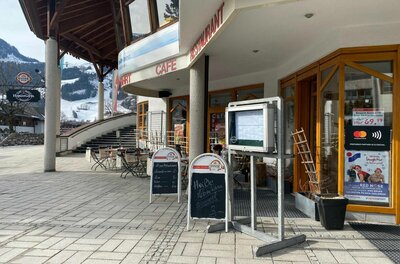 Außenansicht des Restaurants Hornplatzl mit Terrasse, Speisekartenaushängen und Blick auf verschneite Berge.