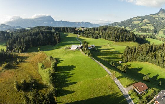Hof Oberhaus in Berglandschaft Luftaufnahme von grünen Wiesen, Wäldern und einzelnen Gehöften vor einer Bergkulisse.
