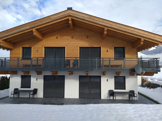 Winterbild Ferienhaus Reiter Zweistöckiges Ferienhaus aus Holz und weißem Putz mit Balkon und Terrasse im Schnee.