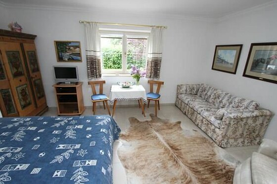 Wohn- und Schlafraum mit Doppelbett, Sofa, Esstisch und rustikalem Schrank.