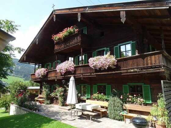 Hausansicht Sommer Lindler Traditionelles Holzhaus mit Blumenbalkonen, grünen Fensterläden und einer Terrasse mit Sitzgelegenheiten.