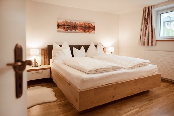 Doppelbett aus hellem Holz mit weißer Bettwäsche in einem modern eingerichteten Schlafzimmer.