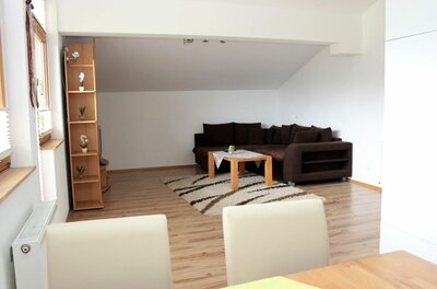 Wohnzimmer mit braunem Ecksofa, Holztisch auf Teppich und hellem Laminatboden unter einer Dachschräge.
