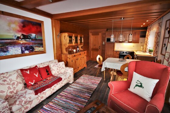 Wohnzimmer der Ferienwohnung Wohn- und Essbereich mit Sofa, rotem Sessel, Holztisch und Küchenzeile in einer Ferienwohnung.
