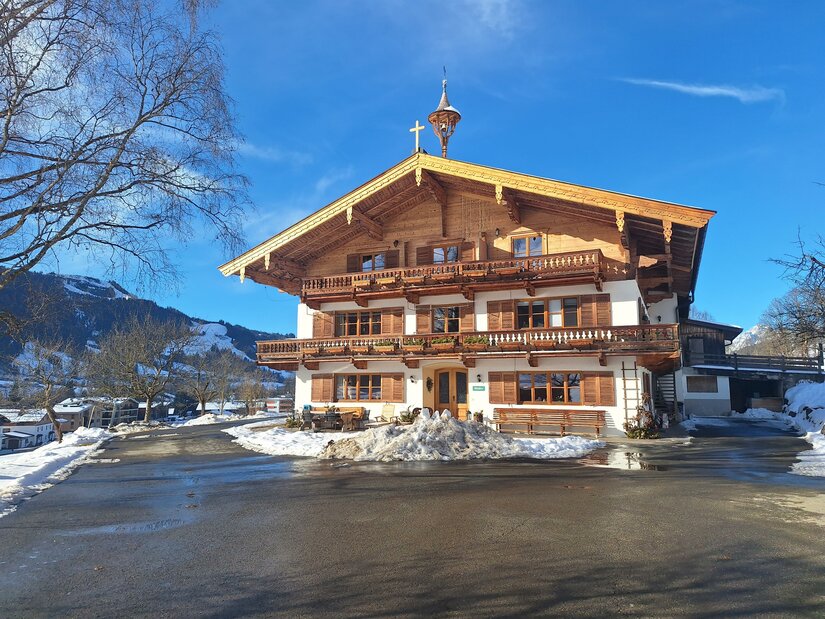 Ein traditionelles Chalet im Winter, umgeben von Schnee. Der Himmel ist blau und die Landschaft ist malerisch.
