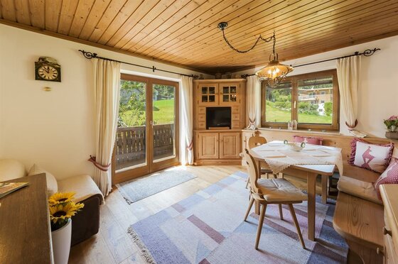 Rustikaler Wohnraum mit Holzdecke, Sitzecke, Esstisch und Balkonzugang.