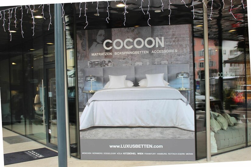 Schaufenster eines Bettengeschäfts mit großem Werbeplakat für Matratzen und Boxspringbetten.