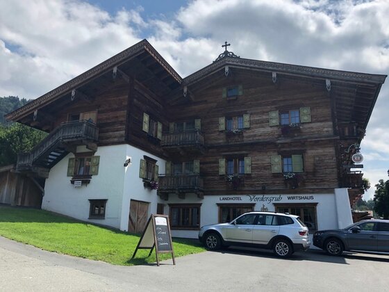 Traditionelles Landhotel aus dunklem Holz mit weißen Fassadenelementen und parkenden Autos davor.