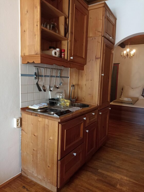 Küchenzeile City Kitz3 Kleine Küchenzeile aus hellem Holz mit Kochfeld, Spüle und Hängeschränken in einem Apartment.