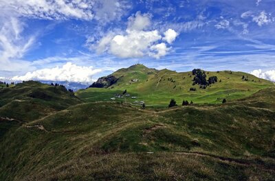 Grüne Hügellandschaft mit Wanderwegen unter blauem Himmel mit weißen Wolken.
