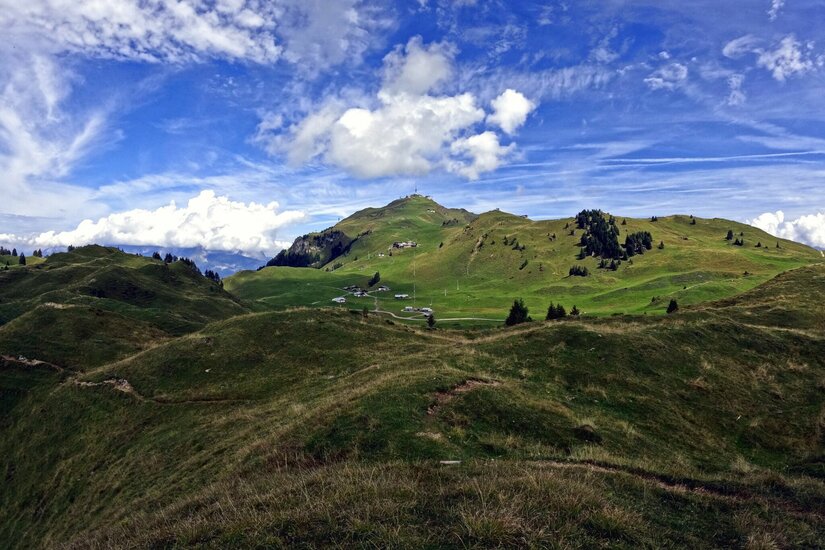 Grüne Hügellandschaft mit Wanderwegen unter blauem Himmel mit weißen Wolken.