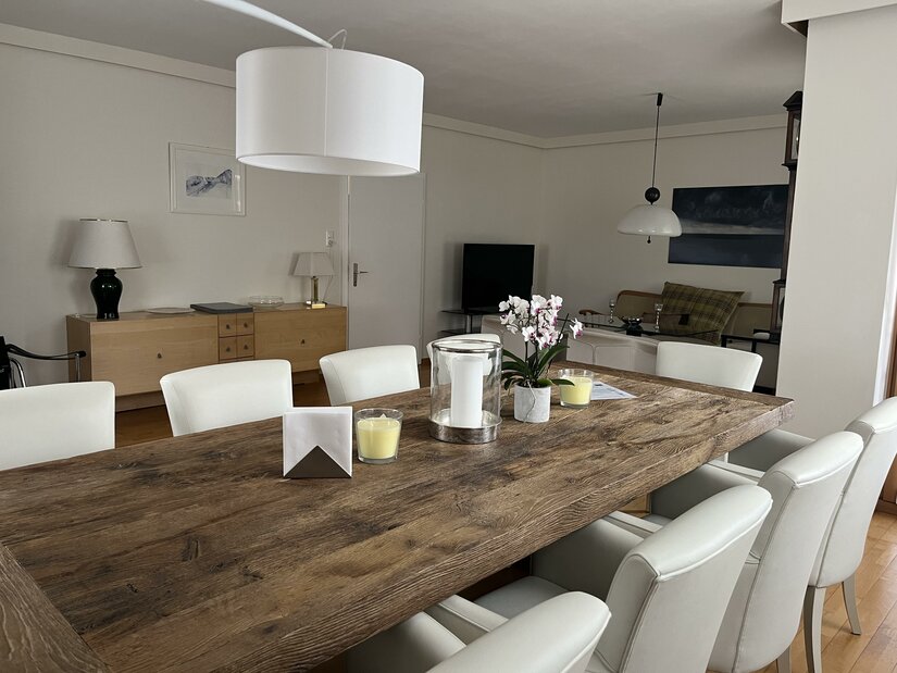 Rustikaler Holztisch mit weißen Lederstühlen in einem hellen Esszimmer.
